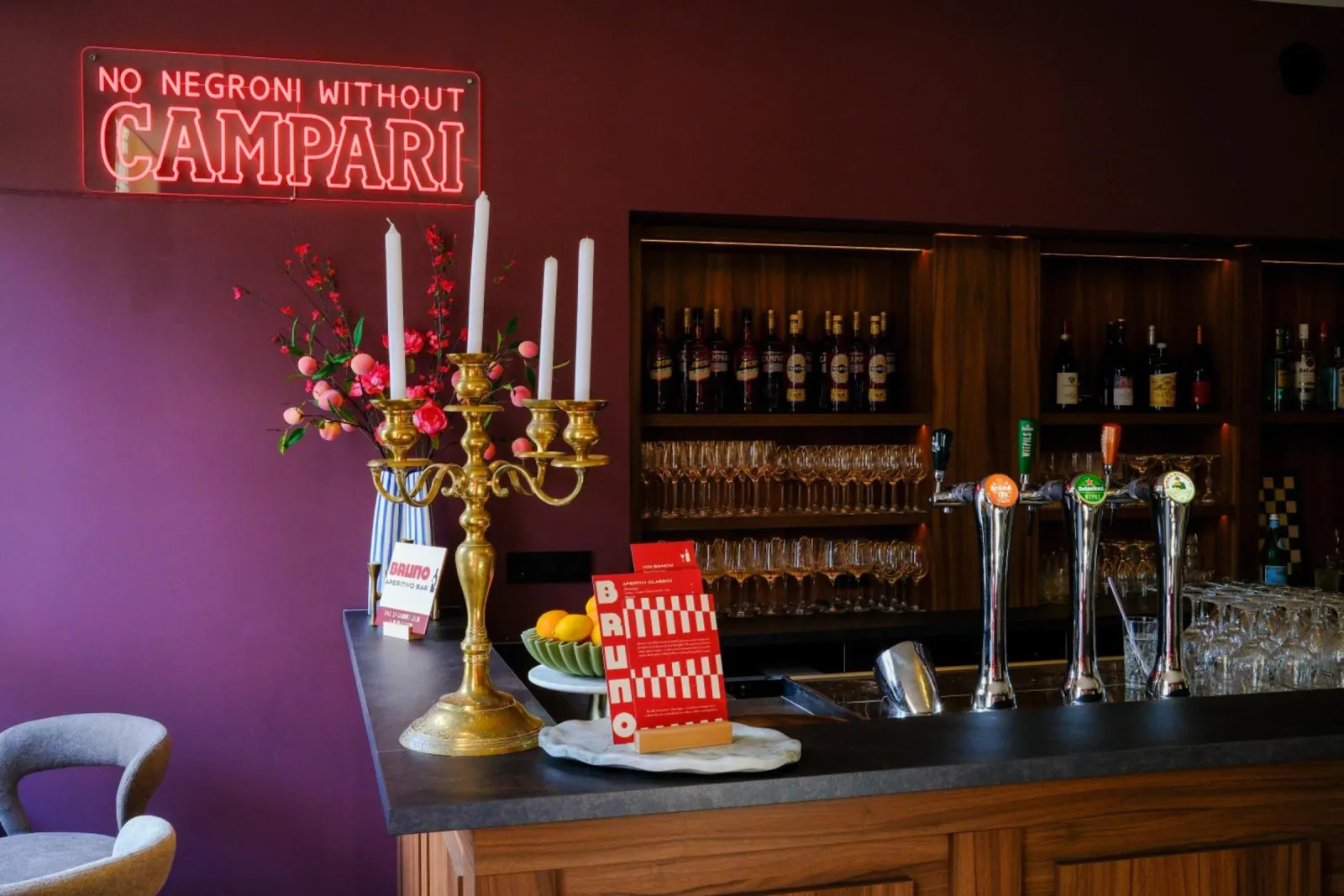 Bruno's bar counter with beer taps, a candelabra and a Campari neon sign against a burgundy wall