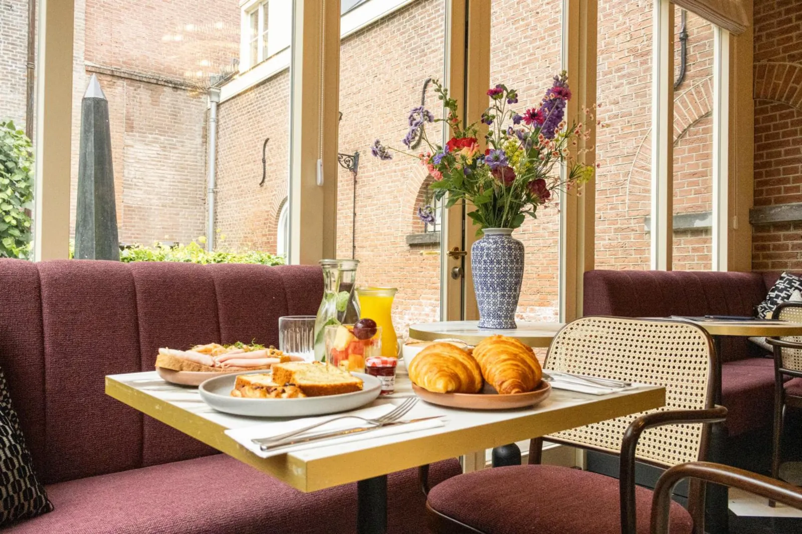 Breakfast table with croissants, cake, juice and a bouquet in the conservatory