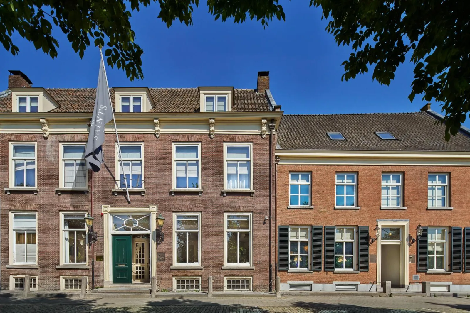Facade of The Saints Den Bosch with its flag, green front door and lanterns