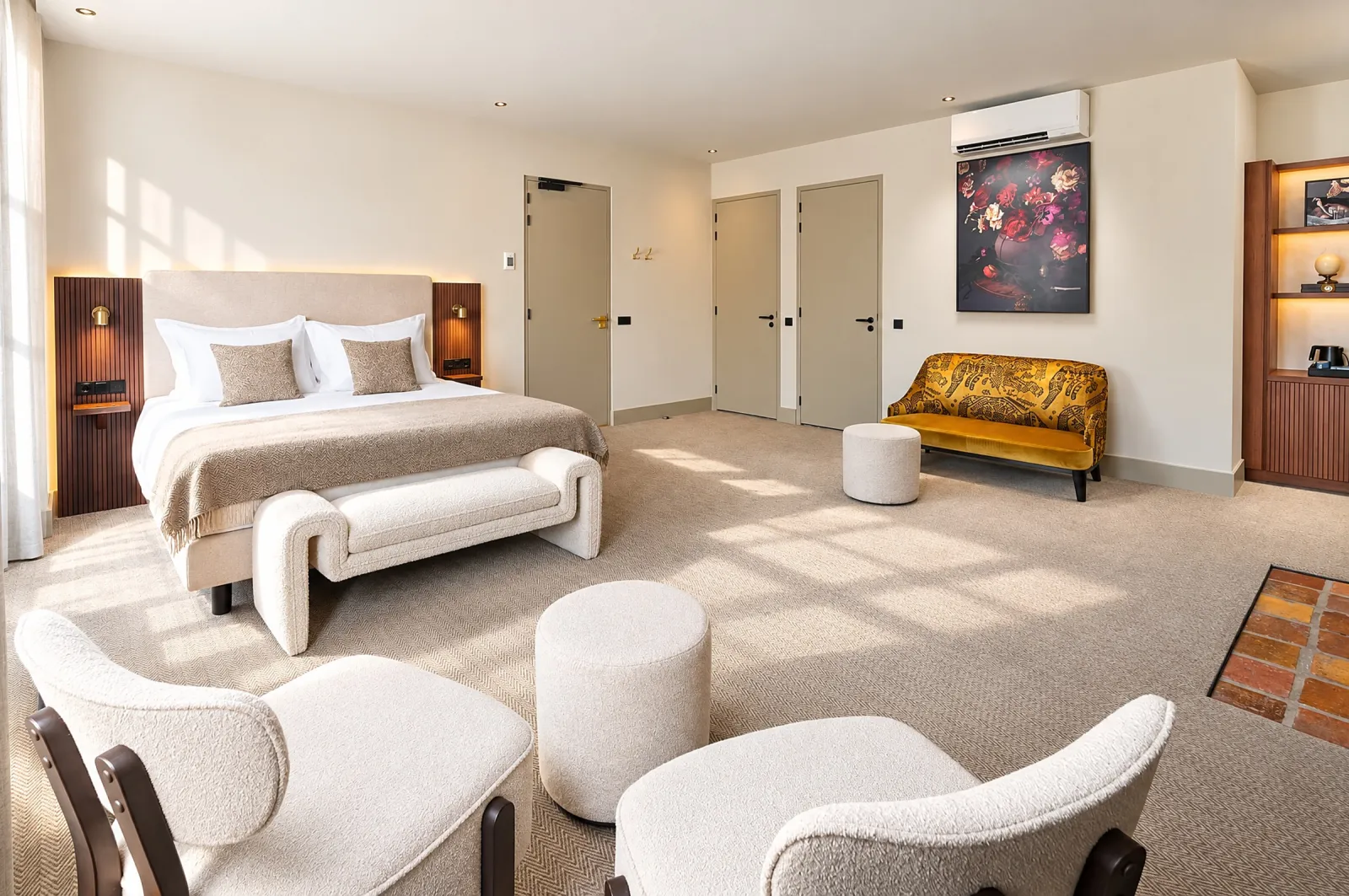 Ruime kamer met bed, bankje, bouclé fauteuils en een okergele bank