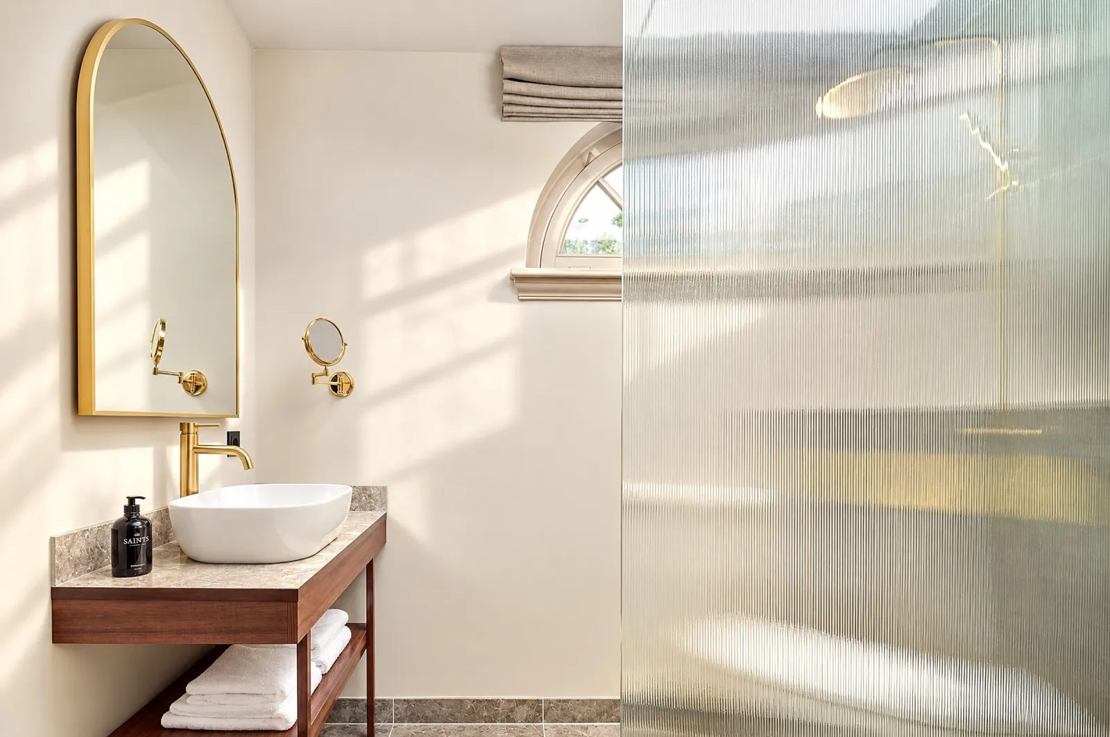 Bathroom with an arched brass mirror, vessel basin, ribbed glass and a round window